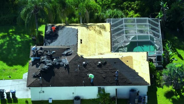 Construction workers removing old asphalt shingles on residential private house roof. Rooftop repair on Florida home. Real estate development concept