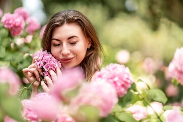 Obraz na płótnie Canvas Hydrangeas Happy woman in pink dress amid hydrangeas. Large pink hydrangea caps surround woman. Sunny outdoor setting. Showcasing happy woman amid hydrangea bloom.