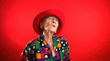 Funny portrait of mature elderly woman, 80s, having giving OKAY gesture, wearing red hat isolated...