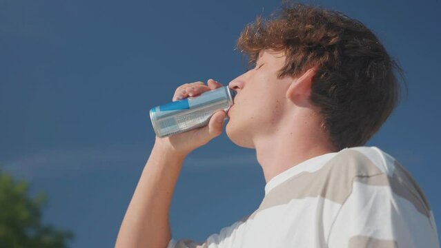 Low angle view of caucasian male drink energy drink during bright summer day