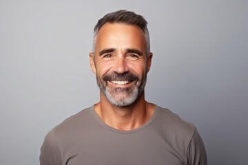 Handsome middle-aged man smiling and looking at camera against grey background