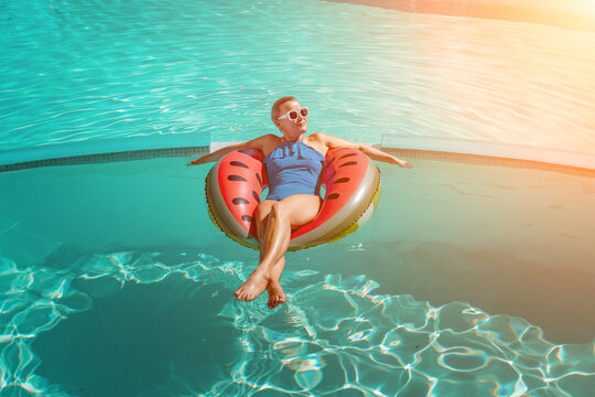Happy woman in a swimsuit and sunglasses floating on an inflatable ring in the form of a watermelon, in the pool during summer holidays and vacations. Summer concept.