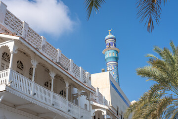 View of a beautiful blue mosque tower with palm tree branches and ornate buildings