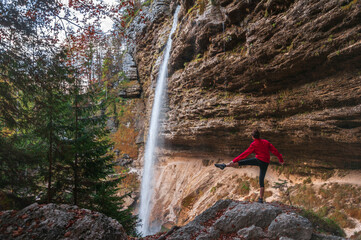 Female Trekker in Red Cloths Stretching Exercises in Front of Waterfall