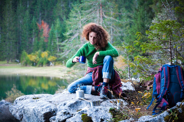 Naklejka na ściany i meble Adventurous Woman Hiker Enjoying a Hot Coffee in Mountains Outdoor Environment Spot near an Alpine Lake