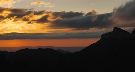 The sky at sunset looks like a layer cake. Silhouettes of mountain peaks. Layered sky, orange, yellow, blue. The beauty of the wilderness.