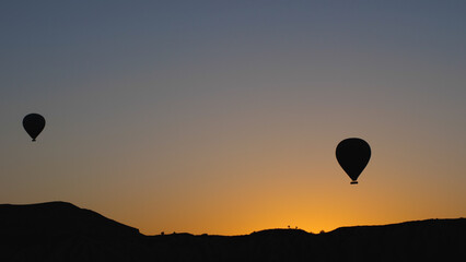 Silhouette of two balloons over a hill. Against the background of the dawn sky. Black and yellow frame. A cinematographic picture of a balloon flight.