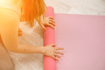 A young woman rolls a pink fitness or yoga mat before or after exercising, exercising at home in...