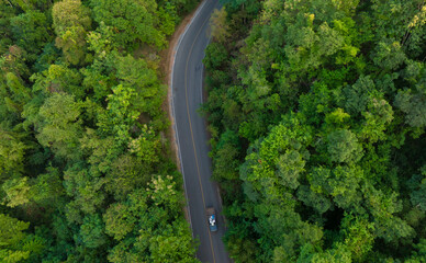 Aerial view of dark green forest road and white electric car Natural landscape and elevated roads Adventure travel and transportation and environmental protection concept