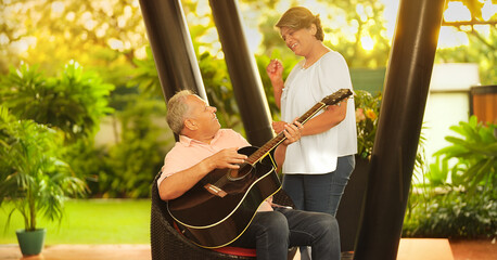 Happy Asian Hindu aged older man male singer sitting on chair play acoustic guitar enjoy day fun...