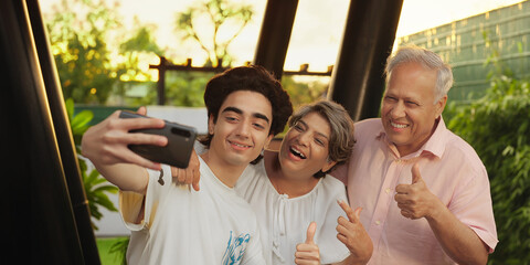 Indian Asian happy old aged mom dad couple pair teen child young adult boy hold mobile use phone look cam take funny face selfie make fun older elder male female lad family enjoy joy home park garden	