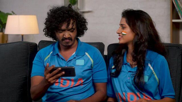 Frustrated Indian fans in jersey while watching live cricket match on mobile phone - concept of entertainment, championship and disappointment.