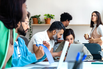 Multiracial coworkers working with laptop in the office. Colleagues have coffee in the background.