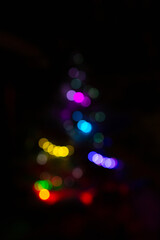 Christmas tree abstract blurred silhouett on black background. Multi-colored vertical lights. Unfocused image with colorful lights on black. Soft focus