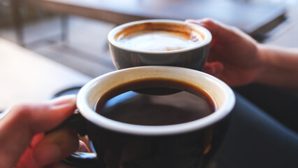 Closeup image of a couple people clinking coffee mugs in cafe