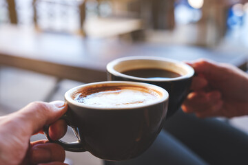 Closeup image of a couple people clinking coffee mugs in cafe