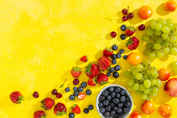 Assortment of different berries on a bright yellow background with copy space. Fresh berries and fruits, green grapes, peaches, strawberries, blueberries. Top view.