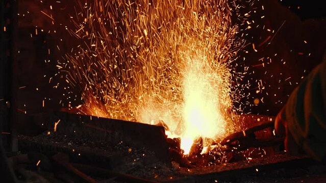 Close-up of a blacksmith's hand, using tongs on a piece of metal, stirring up the fire of the coal forge. Slow motion.