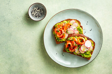 Avocado toasts with salmon, radish, and herbs on a blue plate. Healthy breakfast.