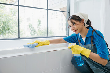 Maid in protective glove uses microfiber cloth for dusting ceramic tiles in bathroom. Her work...