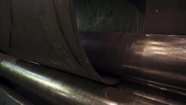 Bending equipment is manufacturing steel tubes at the plant. Tube bending equipment is processing the sheet steel for tube manufacturing. Industrial tube bending equipment in the factory workshop.