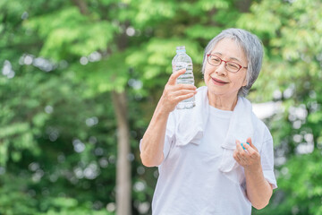 公園で水を飲みながら運動・ウォーキング・歩く高齢者女性
