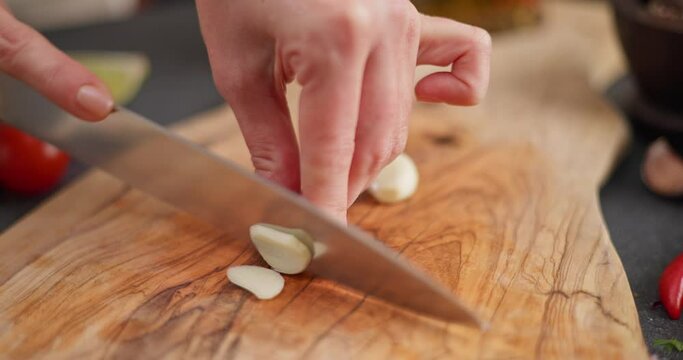 Salsa recipe - Woman cutting and chopping garlic on a wooden board at domestic kitchen