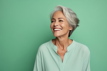Portrait of smiling senior woman in turquoise shirt on green background