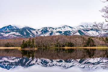 Small islet in the lake, beautiful lake surface reflecting blue sky like a mirror, rolling mountain range and woodland in the background on springtime sunny day. High latitude country natural scenery