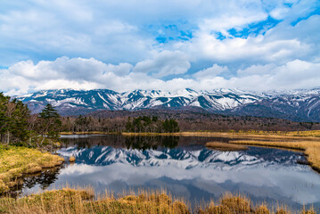 Beautiful lake reflecting blue sky like a mirror, rolling mountain range and woodland in the background on springtime sunny day. High latitude country natural beauty scenery - obrazy, fototapety, plakaty