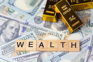 Top view of wealth text on wooden blocks placed on banknotes with gold bars. Financial concepts, saving, investing, and wealth.