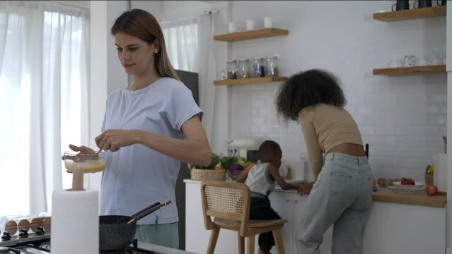 Modern Kitchen Scene, Young Caucasian Woman Frying Eggs, Mother and Son cleaning sink