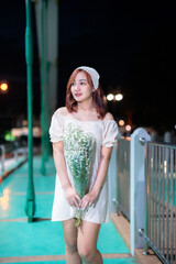 Portrait beautiful asian woman fashion model young red girl wearing summer dress standing holding bouquet on the bridge In the city in the early evening or dusk.