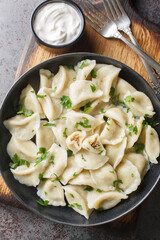 Traditional Polish ravioli dumplings or uszka served with sour cream closeup on the plate on the table. Vertical top view from above