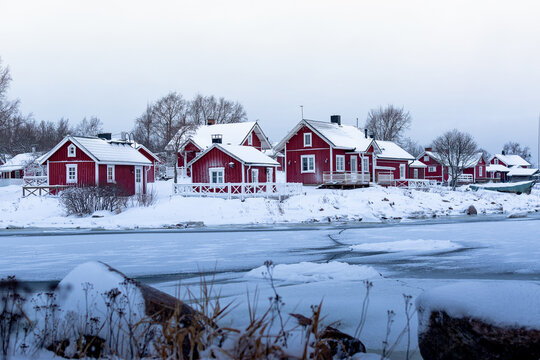 Red wooden houses on the bank of a frozen lake in winter, Finland