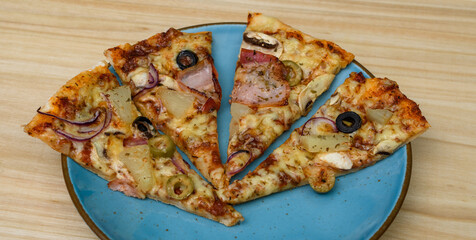 Pizza domowa pokrojona na kawałki leży na niebieskim talerzu na stole - obrazy, fototapety, plakaty