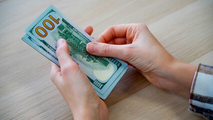 Close-up of unrecognizable female hands counting a stack of American hundred dollar bills....
