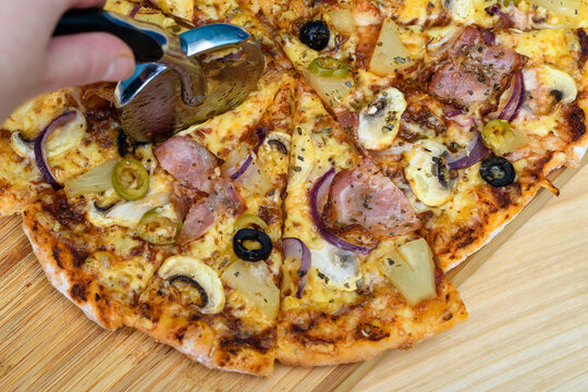 Gorąca pizza krojona nożem do pizzy na tr&oacute;jkątne kawałki, z bliska