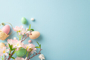 Springtime joy captured: top view miniature basket, vibrant eggs, a sweet bunny, apple blossoms on a pastel blue background. Customizable space for your message