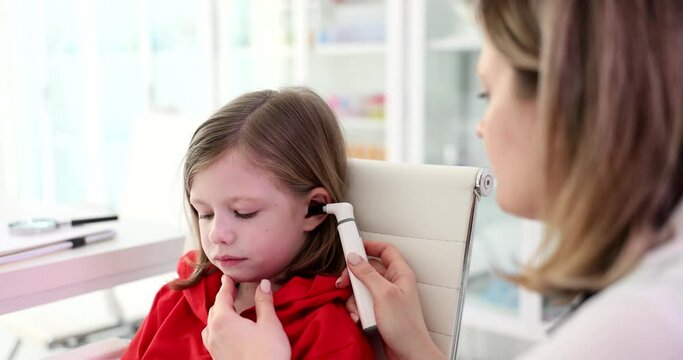 Doctor otorhinolaryngologist examining ear of little girl with otoscope in clinic 4k movie slow motion. Diagnosis and treatment of otitis media and hearing loss in children concept