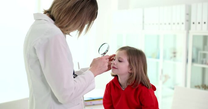 Doctor ophthalmologist examining eye of little girl with magnifying glass in clinic 4k movie slow motion. Foreign body eye diagnosis and treatment concept