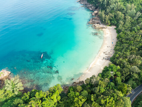 View from above, stunning aerial view of Banana beach, a beautiful white sand beach surrounded by palm trees and bathed by a turquoise water. Phuket, Thailand.