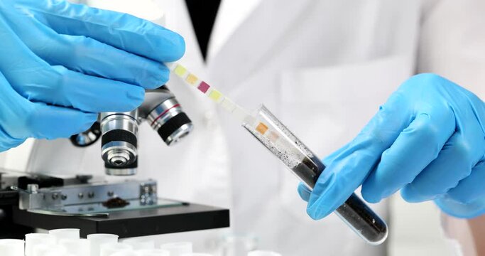 Scientist agronomist chemist inserting litmus paper into test tube with soil closeup 4k movie slow motion. Determination of soil acidity concept
