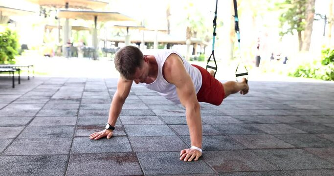 Athlete doing exercises for press on floor with TRX belts in sports field. Sports fitness on in park