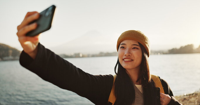Selfie, travel and Japanese woman by lake for holiday, vacation and adventure in Japan. Happy, smile and person take picture on smartphone by water for social media post, memories and online blog