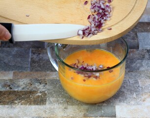 Putting cut red onion into bowl with eggs for omelete. Making egg omelette from fresh organic eggs.