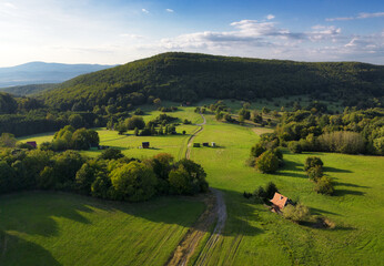 idyllic nature landscape with meadow and cottage in green hills mountain from drone