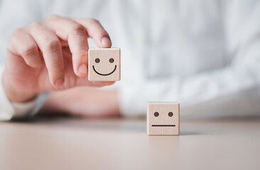 Hand holding smiley happy face on wooden cube and unhappy sad emotion on the floor. World Mental Health Day, Feedback rating, Customer service review. Think positive and satisfaction survey concept.
