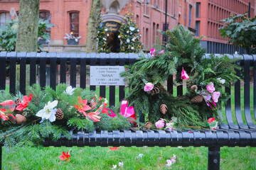 Manchester, United Kingdom - 12 29 2023 : Commemorative plaque in honor of Colin Timmins called "Nana", famous Canal Street drag queen. The bench, in Sackville Gardens, is decorated with flowers