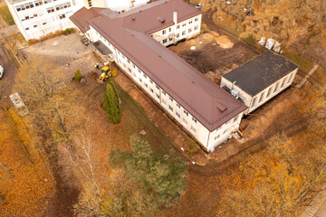 Drone photography of heavy machinery digging dirt around schools foundation and repairing it during autumn day